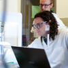 Student researcher in lab. Wearing white lab coat.